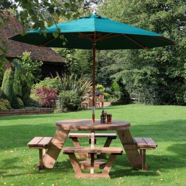 A circular wooden picnic table seating up to 8 people located on a lawn with a green parasol