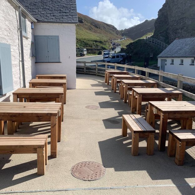Rectangular wooden tables and benches located on a cafe patio at Tintagel Castle