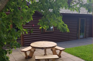 A circular wooden picnic table to seat 6 people on a patio at a holiday park