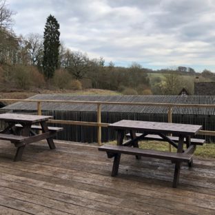 Two brown A frame picnic tables made from recycled plastic on a wooden terrace at Chedworth Roman Villa