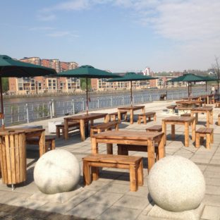 Outdoor wooden rectangular dining tables and benches on a patio at the waters edge of Jurys Inn Hotel Newcastle