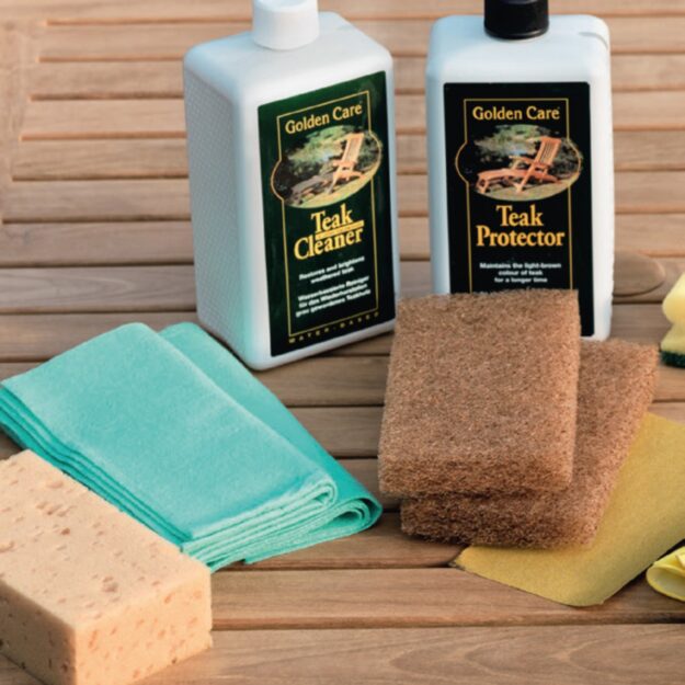 A teak outdoor furniture care kit with treatment fluid bottle and cloths and sponges laid out on a wooden table