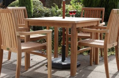 A square teak outdoor dining table and four stacking armchairs around it on a patio