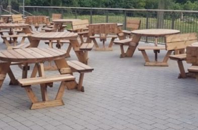 A large patio full of socially distanced 2m apart round wooden picnic tables