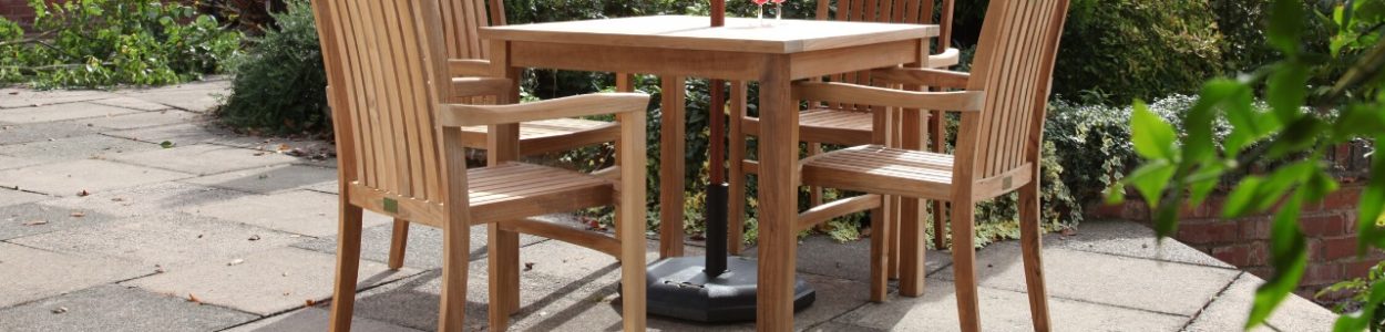 A square teak outdoor table and 4 matching dining armchairs on a patio