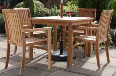 A square teak outdoor table and 4 matching dining armchairs on a patio