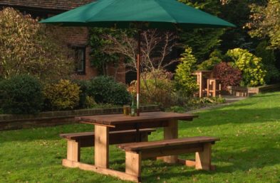 A 4 seater wooden picnic table on a lawn with a green parasol