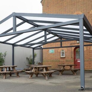 A grey metal framed gazebo with an apex roof made from polycarbonate with picnic tables underneath it