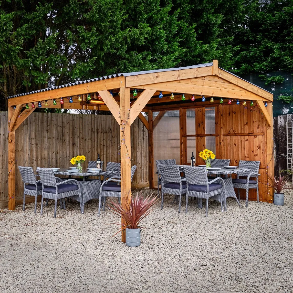 A wooden gazebo with grey rattan outdoor tables and chairs underneath it on a gravel patio