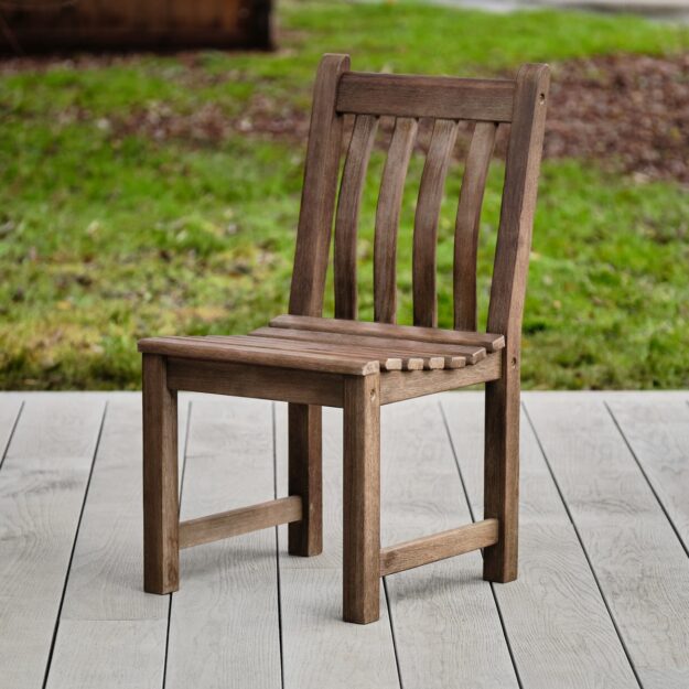 A hard wood outdoor dining chair with slatted back and seat on a garden deck