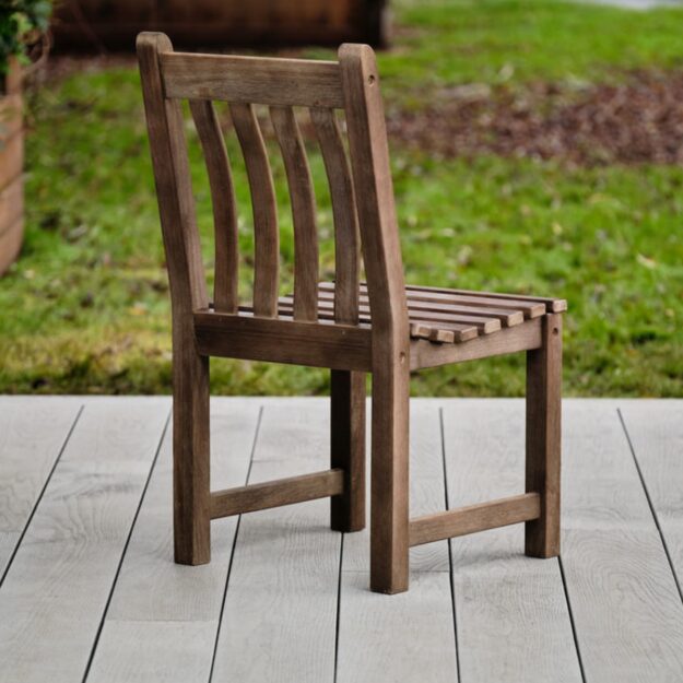 A hard wood outdoor dining chair with slatted back showing the back view of the chair on a garden deck