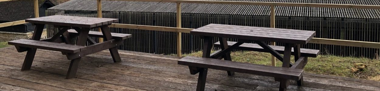 Two brown recycled plastic a frame picnic tables on a wooden deck over looking Chedworth roman villa