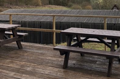 Two brown recycled plastic a frame picnic tables on a wooden deck over looking Chedworth roman villa