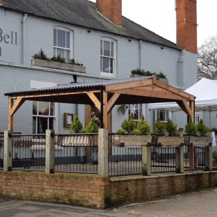 A square wooden gazebo with a waterproof roof on the front patio of a country pub
