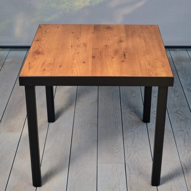 A square outdoor dining table made from aluminium frame and laminate wood effect table top located on a grey outdoor deck