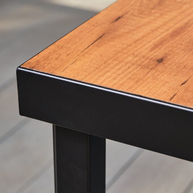 A corner of a square outdoor dining table showing a curved soft edge corner frame made from dark grey aluminium and table top from laminate wood effect