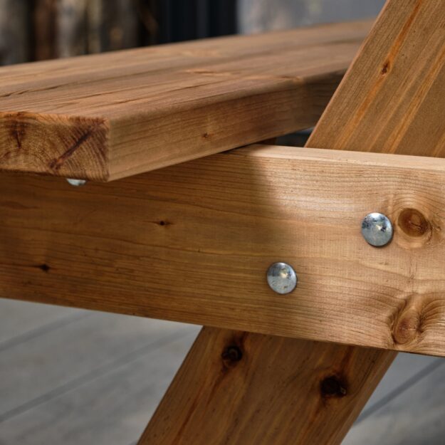 A zoomed in photo of the seat join on a wooden a frame picnic table with heavy duty metal bolts