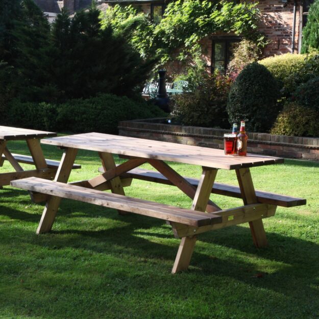 A 2 metre long wooden A frame picnic table on a lawn with bottles of beer and a pint glass on top