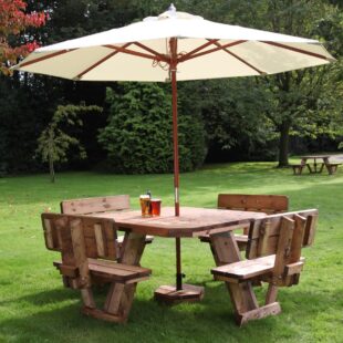A square wooden 8 seater picnic table with seat backrests and a cream parasol on a lawn