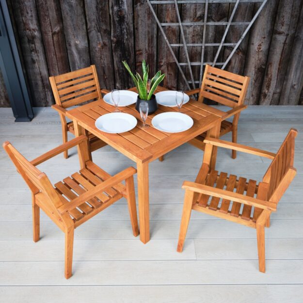 An overhead and side view of a square robinia hardwood outdoor dining table and 4 chairs with plates, glasses and a pot plant on a grey outdoor deck