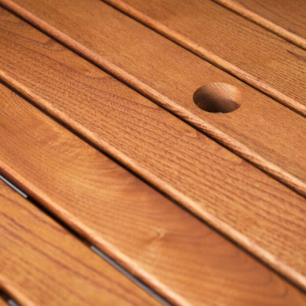 A close up of an outdoor hardwood table top with parasol hole