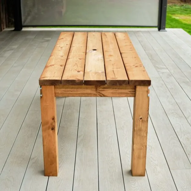 An end on view of a rectangular chunky wooden outdoor dining table on a grey deck