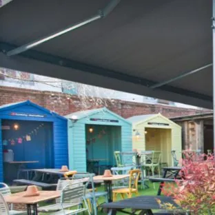 Brightly coloured wooden cabins that look like beach huts in a pub garden for people to sit in undercover