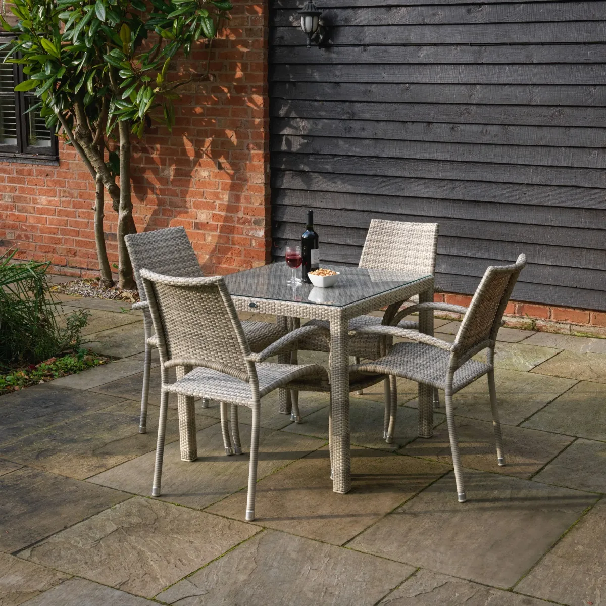A square cream grey rattan weave outdoor dining table and matching armchairs on a patio