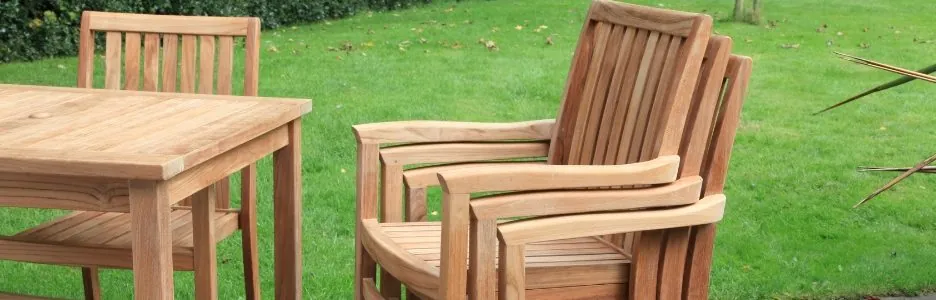 A stack of 3 teak outdoor chairs next to a square teak outdoor table on a patio